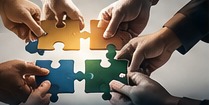 Hands joining puzzle pieces to represent workplace collaboration.